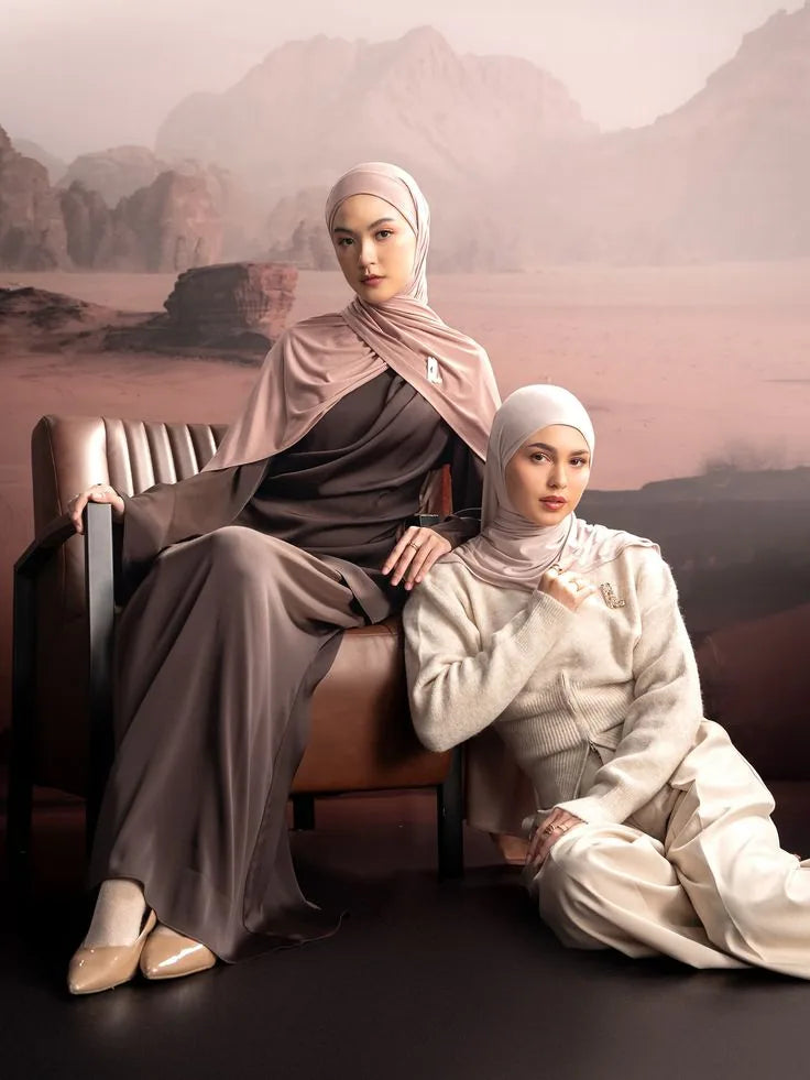 Two models in satin abayas against a desert backdrop